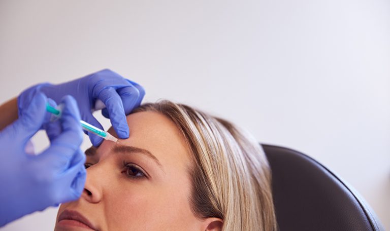 Woman Sitting In Chair Being Give Botox Injection In Forehead By Female Doctor